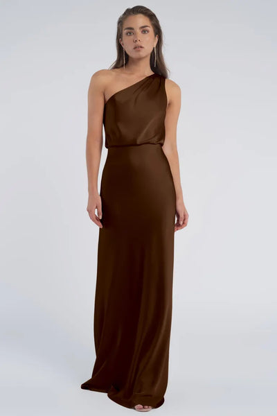Woman in a long, Jenny Yoo Bridesmaid dress with a one-shoulder neckline standing against a neutral background.