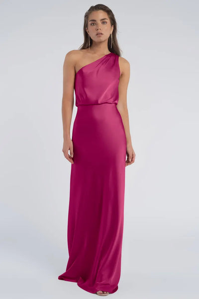 A woman in an elegant, one-shoulder fuchsia gown crafted from luxe satin fabric, Sterling by Jenny Yoo Bridesmaid, stands against a neutral background at Bergamot Bridal.
