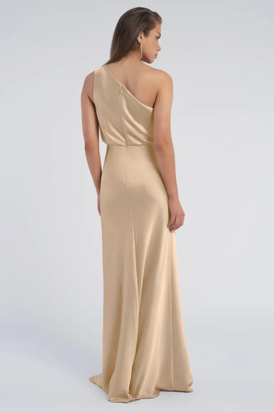 Woman wearing an elegant Sterling - Jenny Yoo Bridesmaid gold evening gown with a one-shoulder neckline, viewed from the back, by Bergamot Bridal.