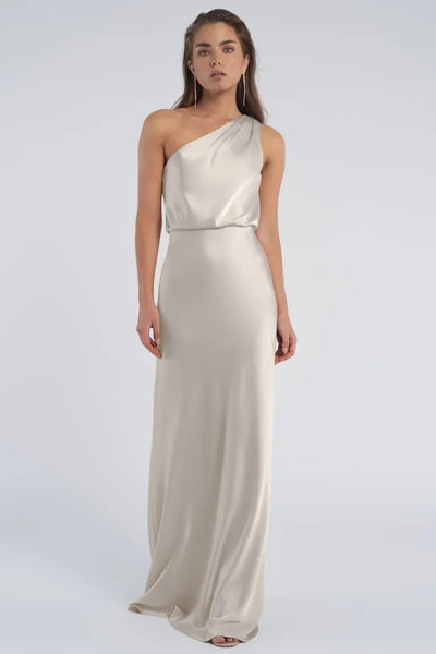 Woman in an elegant one-shoulder Jenny Yoo Bridesmaid dress standing against a neutral background.