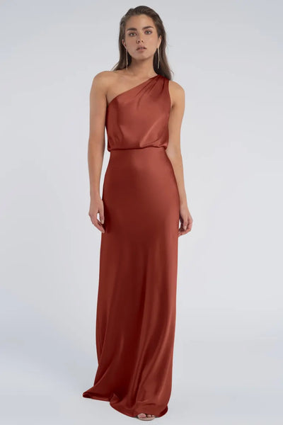 A woman in an elegant red evening gown with a one-shoulder neckline from Sterling - Jenny Yoo Bridesmaid stands against a neutral background.