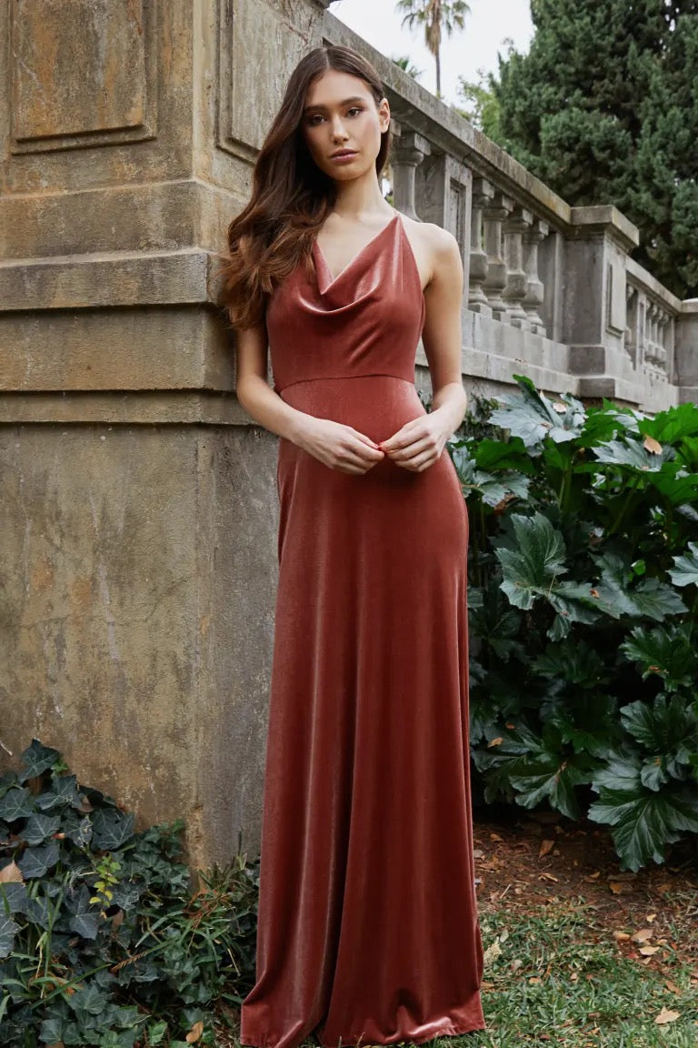 Woman in a long, elegant Sullivan - Bridesmaid Dress by Jenny Yoo standing by a stone wall with green foliage around, from Bergamot Bridal.