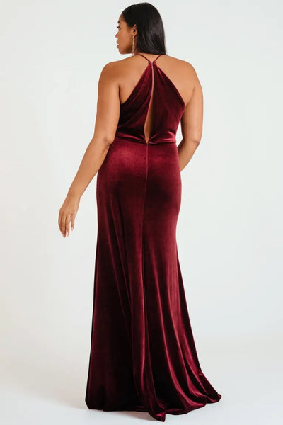 Woman in an elegant Sullivan bridesmaid dress by Jenny Yoo in burgundy velvet with a halter cowl neckline, viewed from behind from Bergamot Bridal.