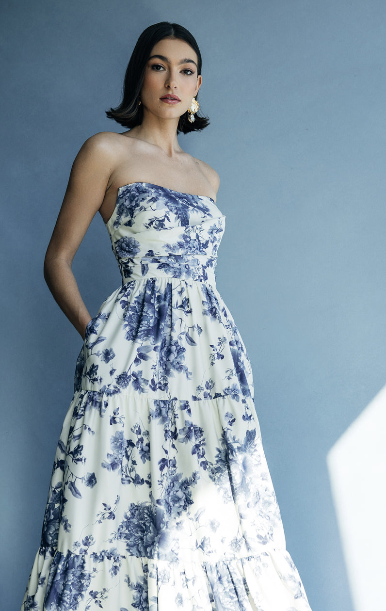 Woman standing in a blue and white floral Sutton dress with detachable puff sleeves against a gray backdrop - Bergamot Bridal's Jenny Yoo Bridesmaid Dress.