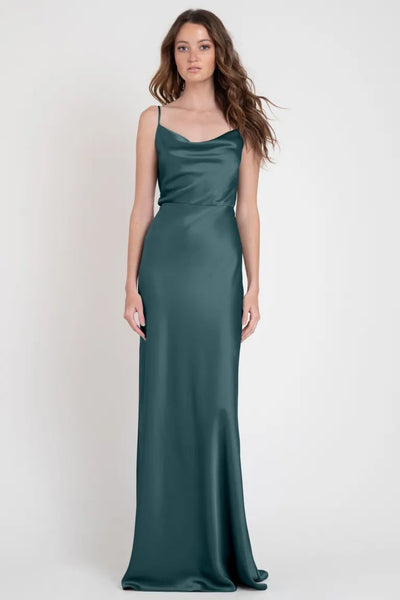 A woman modeling a stylish, long satin teal evening gown with a one-shoulder neckline, the Sylvie - Bridesmaid Dress by Jenny Yoo from Bergamot Bridal.