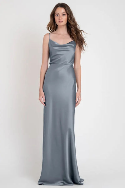 A woman in a Sylvie - Bridesmaid Dress by Jenny Yoo standing against a neutral backdrop, exuding an Old Hollywood elegance.