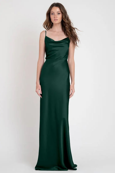 A woman models the Sylvie - Bridesmaid Dress by Jenny Yoo, a floor-length, dark green satin evening gown with a sleeveless design, embodying Old Hollywood glamour from Bergamot Bridal.