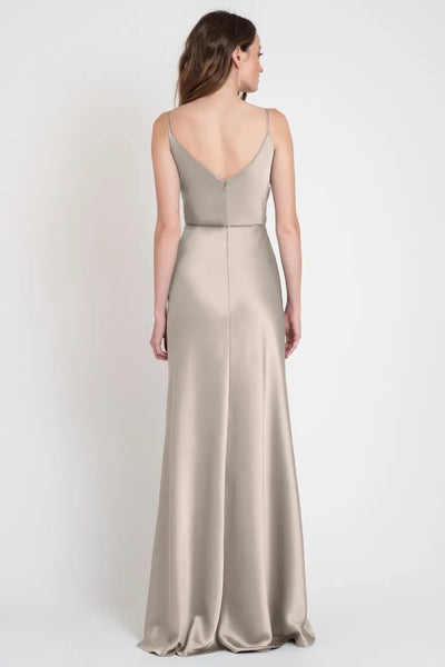 A woman from behind wearing a long, elegant beige Sylvie - Bridesmaid Dress by Jenny Yoo with slender straps from Bergamot Bridal.