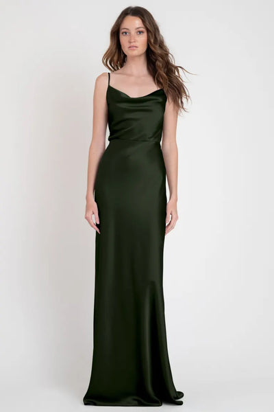 A woman stands against a white background wearing the Sylvie - Bridesmaid Dress by Jenny Yoo from Bergamot Bridal, a stylish dark green satin slip dress with thin straps that evokes the glamor of Old Hollywood.