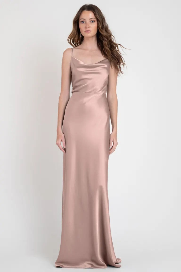 A woman modeling a Sylvie - Bridesmaid Dress by Jenny Yoo, a long satin blush-colored evening gown giving off Old Hollywood vibes from Bergamot Bridal.