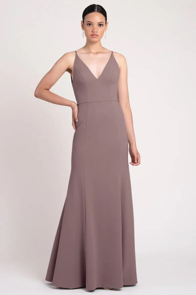 Woman in an elegant Taryn - Bridesmaid Dress by Jenny Yoo gown with slimming seam lines and a v-neckline standing against a neutral background. (Brand: Bergamot Bridal)