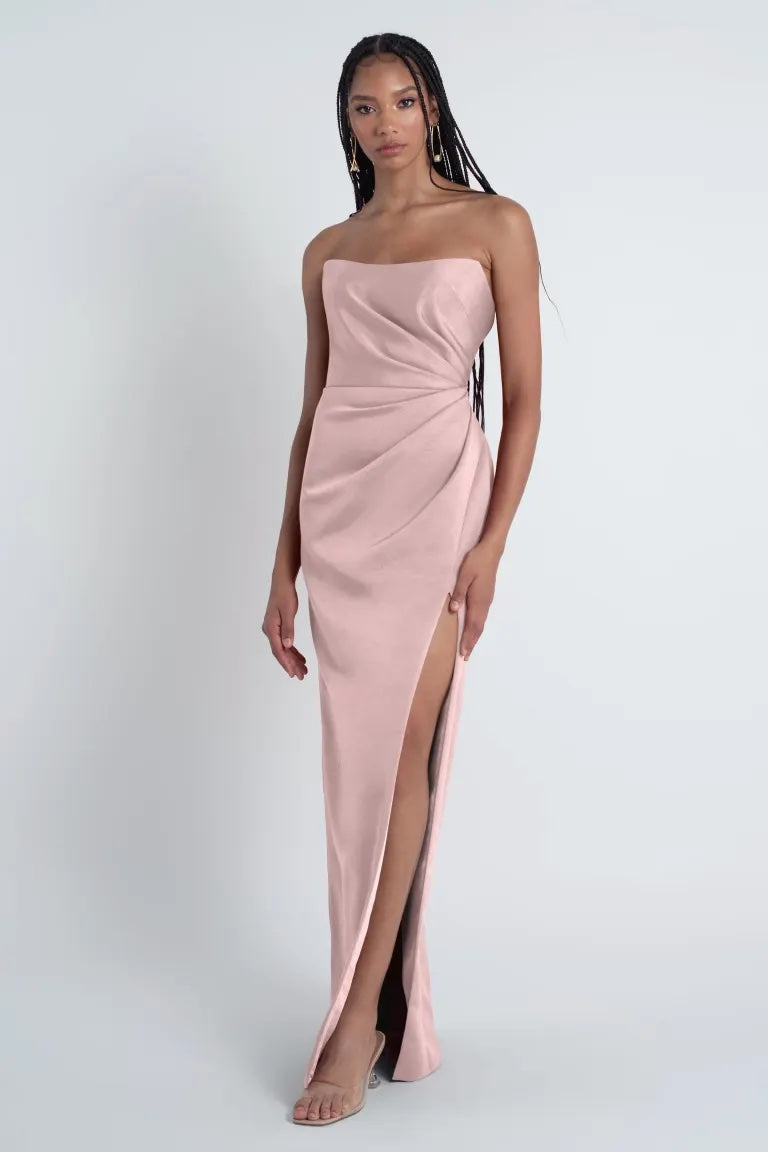 A woman wearing a pink strapless Waverly - Jenny Yoo Bridesmaid Dress with a thigh-high slit from Bergamot Bridal.