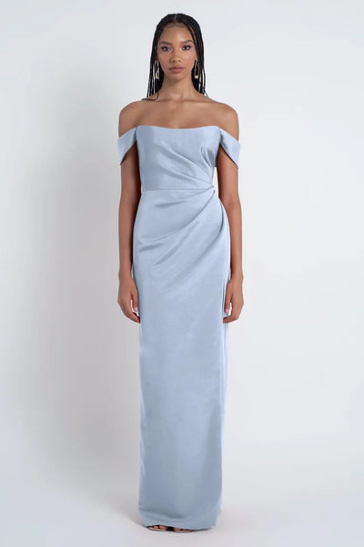 A woman wearing an off-the-shoulder Jenny Yoo Bridesmaid Dress stands against a white background from Bergamot Bridal.