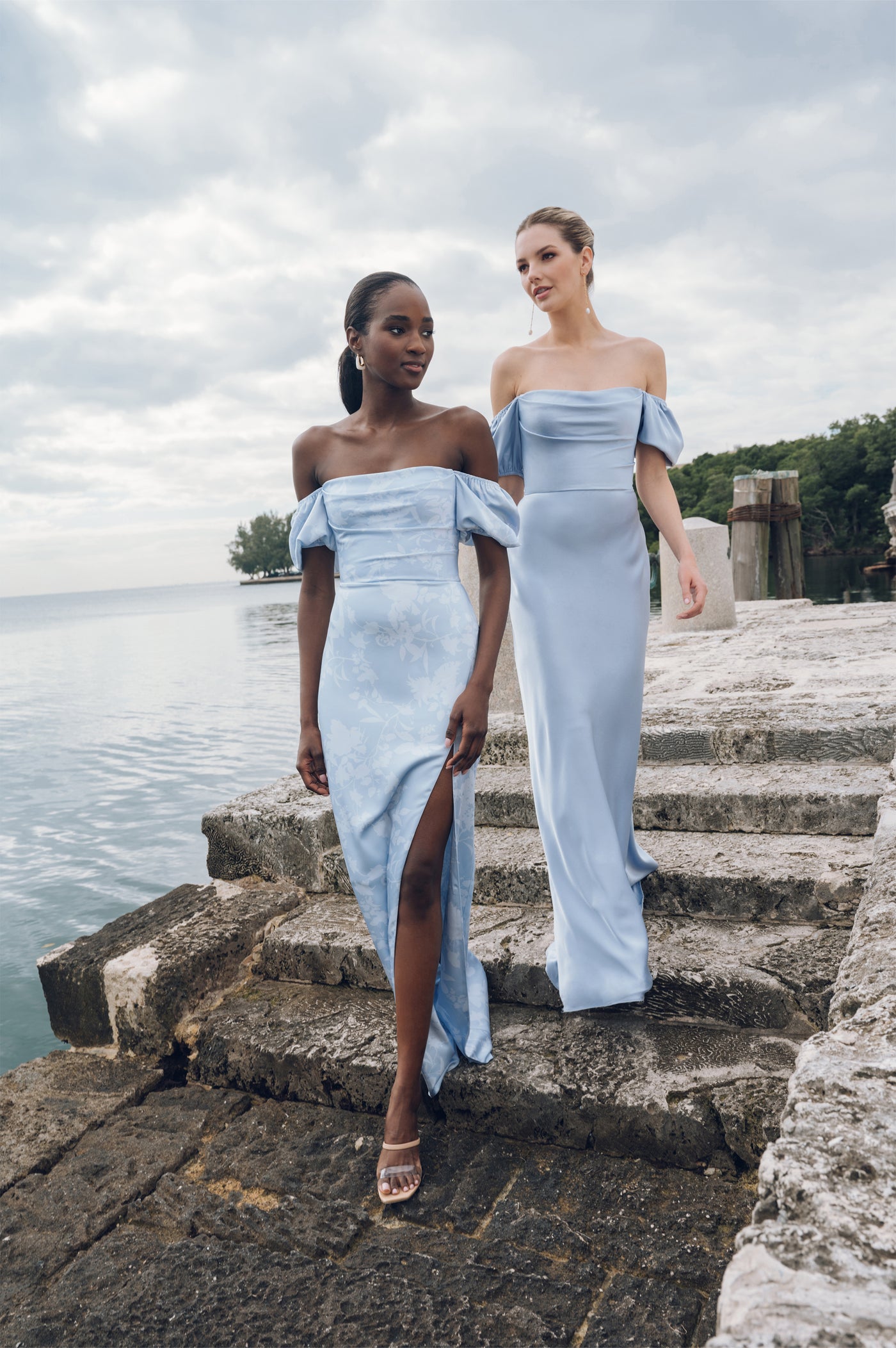 Two women in elegant Jenny Yoo Bridesmaid Dresses from Bergamot Bridal posing by the waterfront.