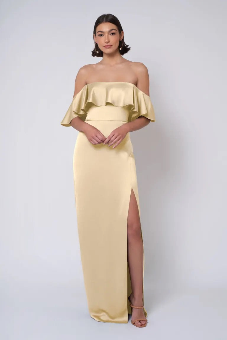 Woman posing in an elegant strapless off-shoulder yellow Winter - Jenny Yoo Bridesmaid Dress gown with a thigh-high slit from Bergamot Bridal.