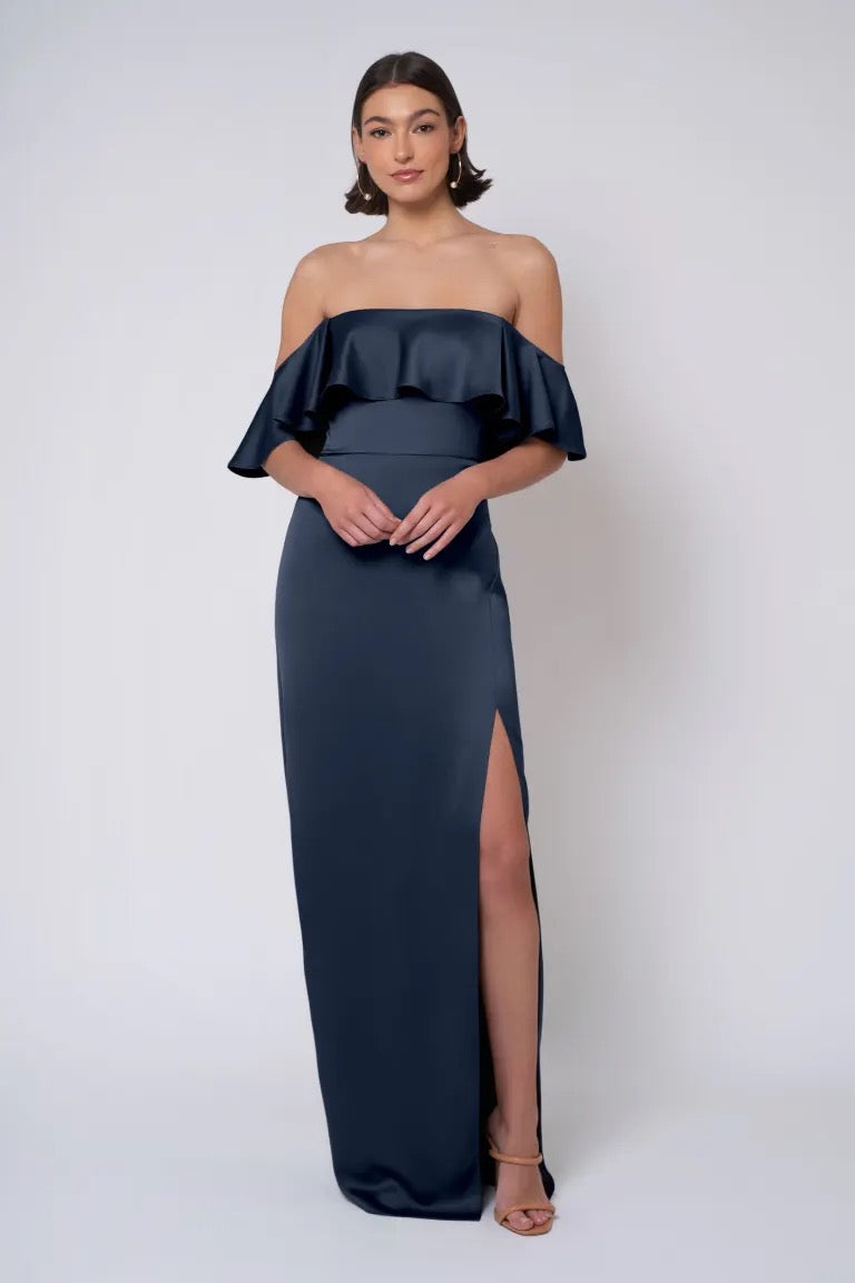 Woman in an elegant Winter - Jenny Yoo Bridesmaid Dress from Bergamot Bridal, featuring a navy blue strapless neckline and off-the-shoulder style with a high slit.