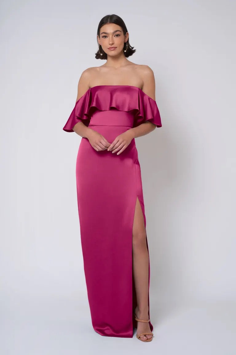 A woman in a Winter - Jenny Yoo Bridesmaid Dress with a magenta strapless neckline and high leg slit stands against a white background from Bergamot Bridal.