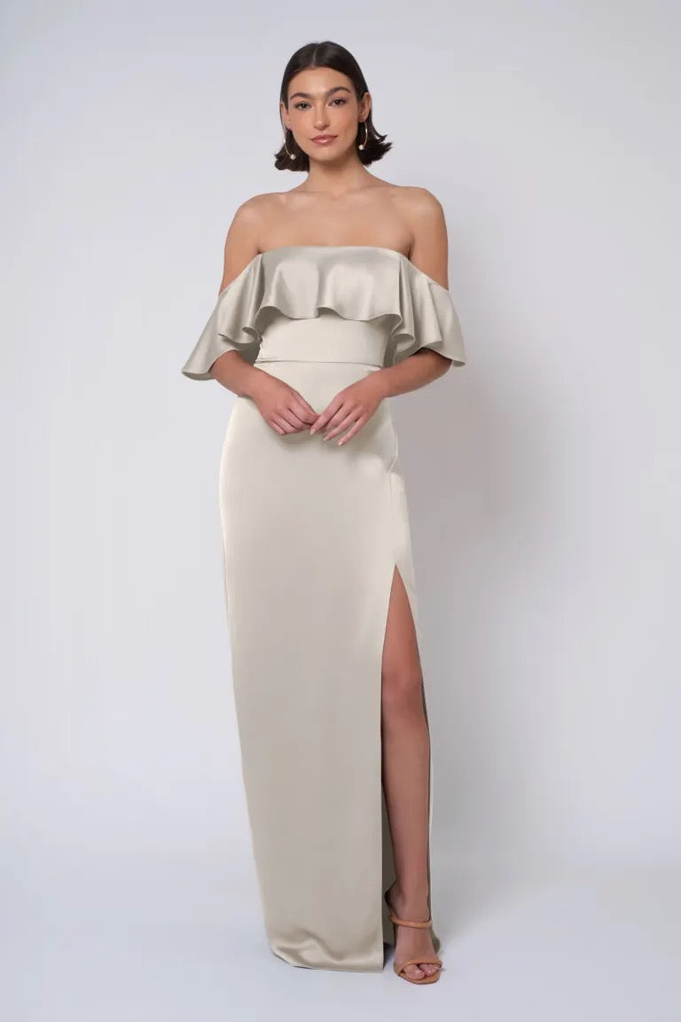 A woman posing in an elegant Winter - Jenny Yoo Bridesmaid Dress gown with a ruffle neckline and thigh-high slit from Bergamot Bridal.