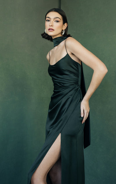 Elegant woman posing in a sleek black satin Wren - Jenny Yoo bridesmaid dress with a high slit from Bergamot Bridal.