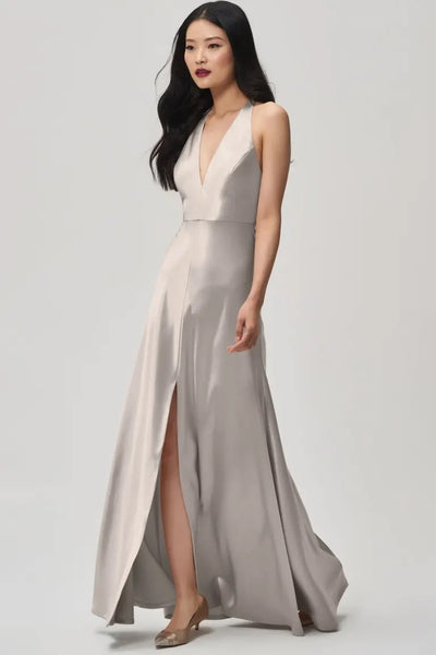Woman in an elegant Corinne satin back crepe bridesmaid dress by Jenny Yoo with a plunging halter V-neck, posing against a neutral background from Bergamot Bridal.