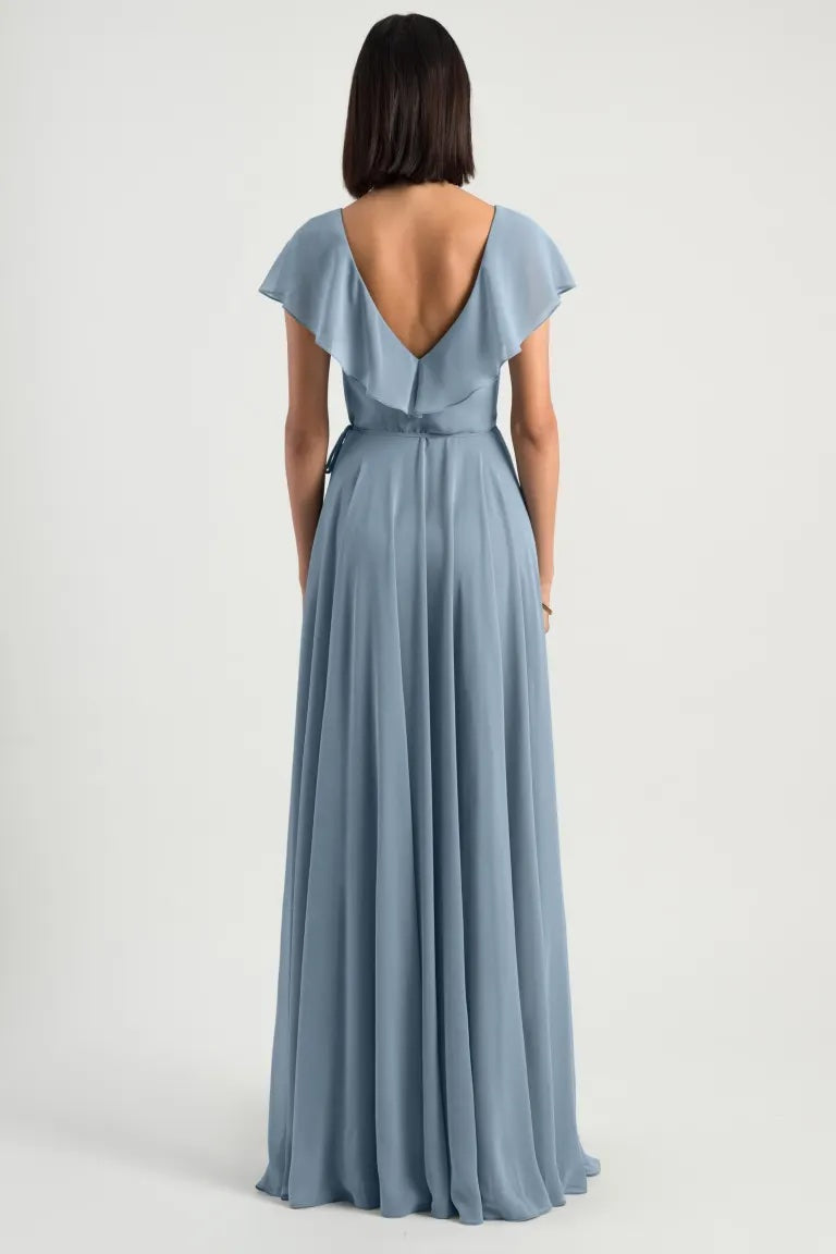 A woman from behind wearing an elegant blue Faye Bridesmaid Dress by Jenny Yoo with a deep v-back, flutter sleeve, and flowing skirt from Bergamot Bridal.