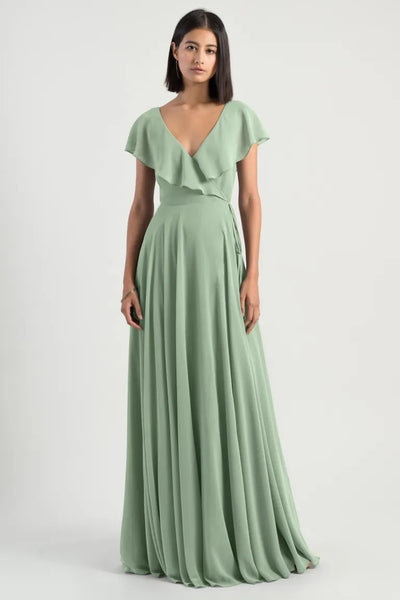 Woman posing in an elegant sage green chiffon wrap dress with a v-neckline, the Faye Bridesmaid Dress by Jenny Yoo from Bergamot Bridal.
