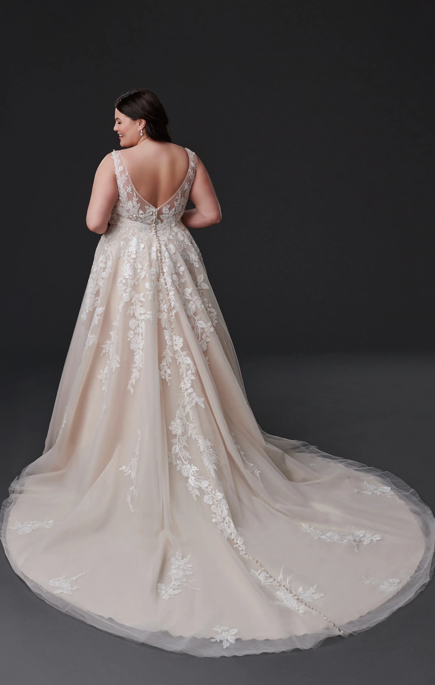 A woman in an elegant Eddy K Geneva - Off The Rack A-line wedding dress with intricate lace detailing and floral appliqués seen from the back at Bergamot Bridal.