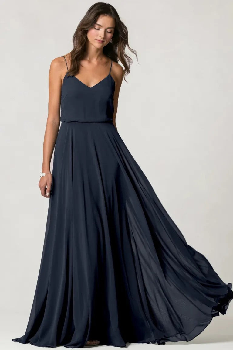 Woman posing in an elegant navy blue Inesse bridesmaid dress by Jenny Yoo with a flowing skirt and spaghetti straps from Bergamot Bridal.