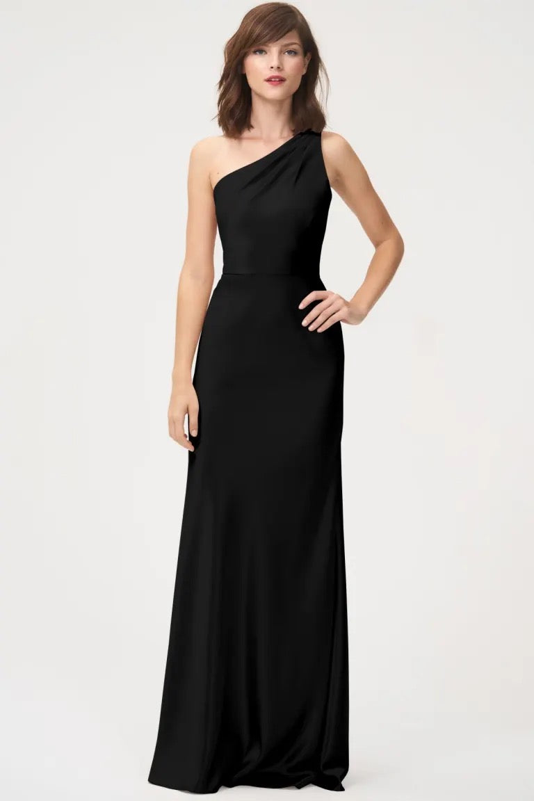 Woman modeling a black one-shoulder evening gown, known as the Lena dress by Jenny Yoo, featuring a satin back crepe finish.
