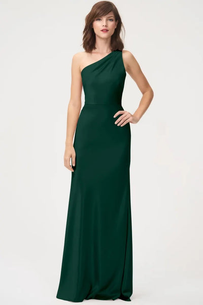 A woman in an elegant green Lena - Bridesmaid Dress by Jenny Yoo with a one-shoulder neckline poses with her hand on her hip from Bergamot Bridal.