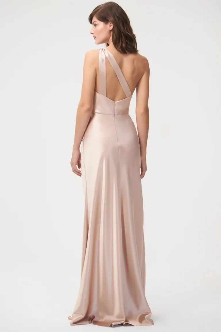 Woman in an elegant, blush-toned Lena - Bridesmaid Dress by Jenny Yoo made of satin back crepe, featuring a one-shoulder neckline from Bergamot Bridal.