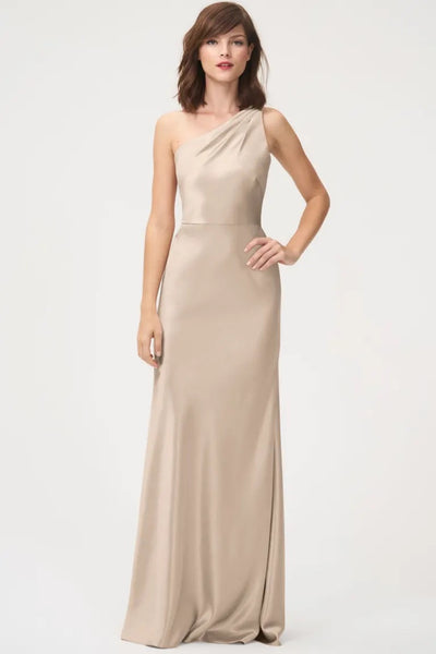 A woman in an elegant beige Lena Bridesmaid Dress by Jenny Yoo with a satin back crepe texture, posing against a plain background from Bergamot Bridal.