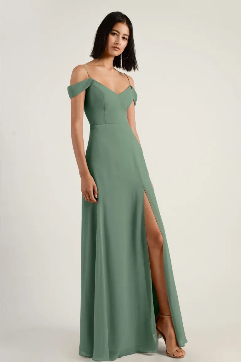 A woman in an elegant green chiffon Priya bridesmaid dress by Jenny Yoo with a V-neck and a high side slit from Bergamot Bridal.