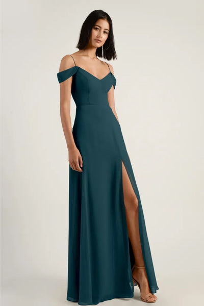 Woman posing in an elegant teal Priya V-neck chiffon bridesmaid dress by Jenny Yoo with a high slit and off-the-shoulder straps from Bergamot Bridal.