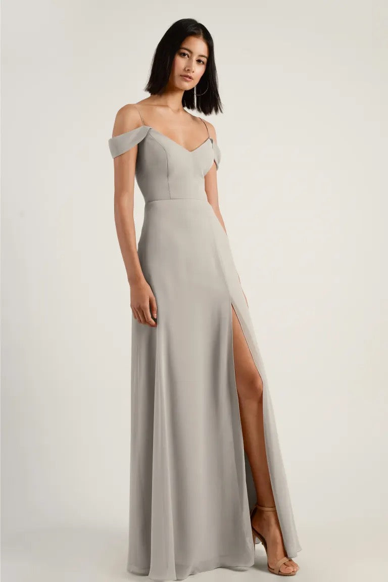 Woman posing in an elegant off-the-shoulder gray Priya - Bridesmaid Dress by Jenny Yoo with a thigh-high slit and V-neck from Bergamot Bridal.
