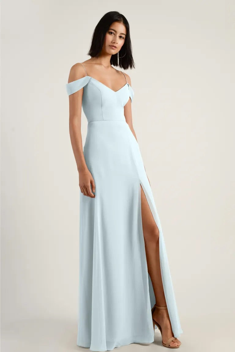 A woman models a Priya bridesmaid dress in light blue with off-the-shoulder straps and a high leg slit by Jenny Yoo from Bergamot Bridal.