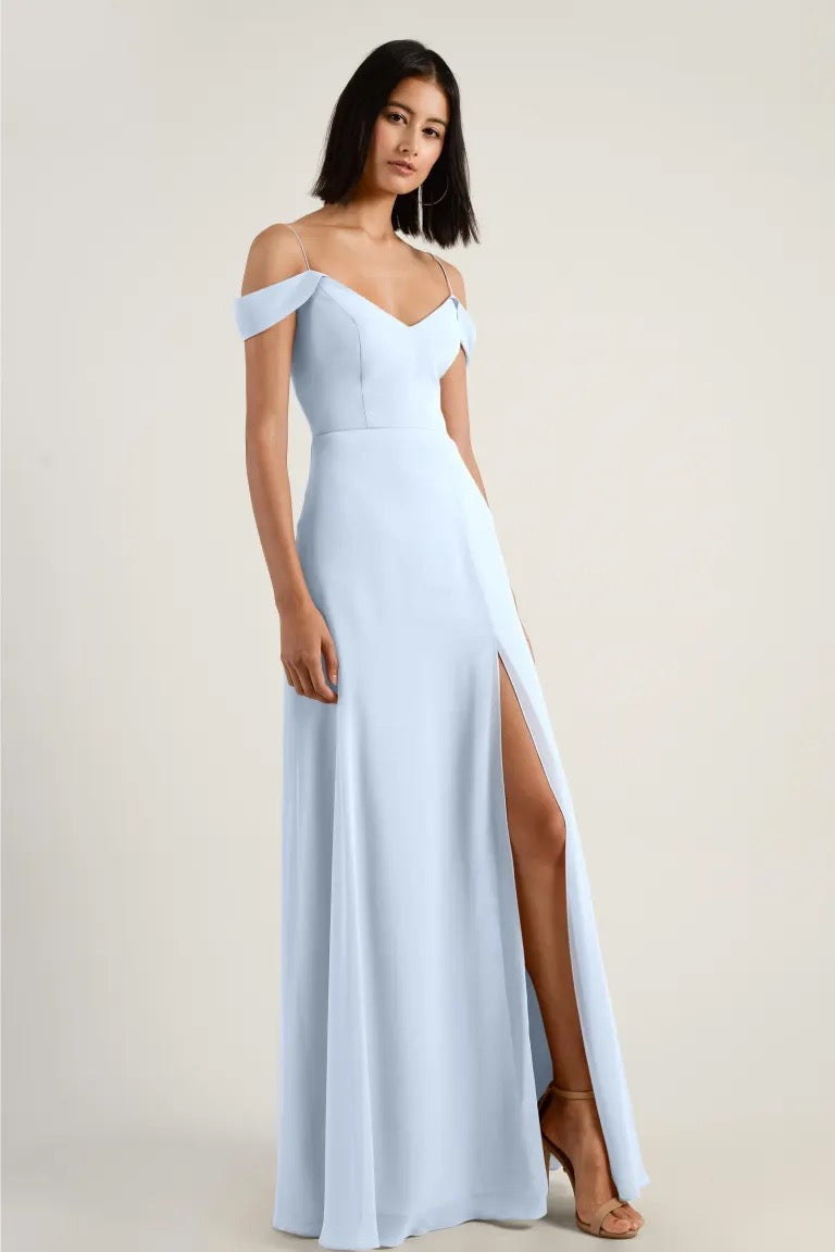 Woman posing in an elegant light blue chiffon bridesmaid dress with a high side slit and off-shoulder straps, the Priya - Bridesmaid Dress by Jenny Yoo from Bergamot Bridal.