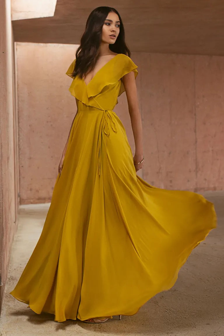 Woman in an elegant yellow chiffon wrap dress with a flutter sleeve and full circle skirt - Faye - Bridesmaid Dress by Jenny Yoo from Bergamot Bridal.