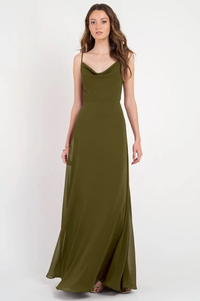 A woman in a long olive green Colby - Jenny Yoo Bridesmaid Dress with a cowl neckline standing against a white background from Bergamot Bridal.