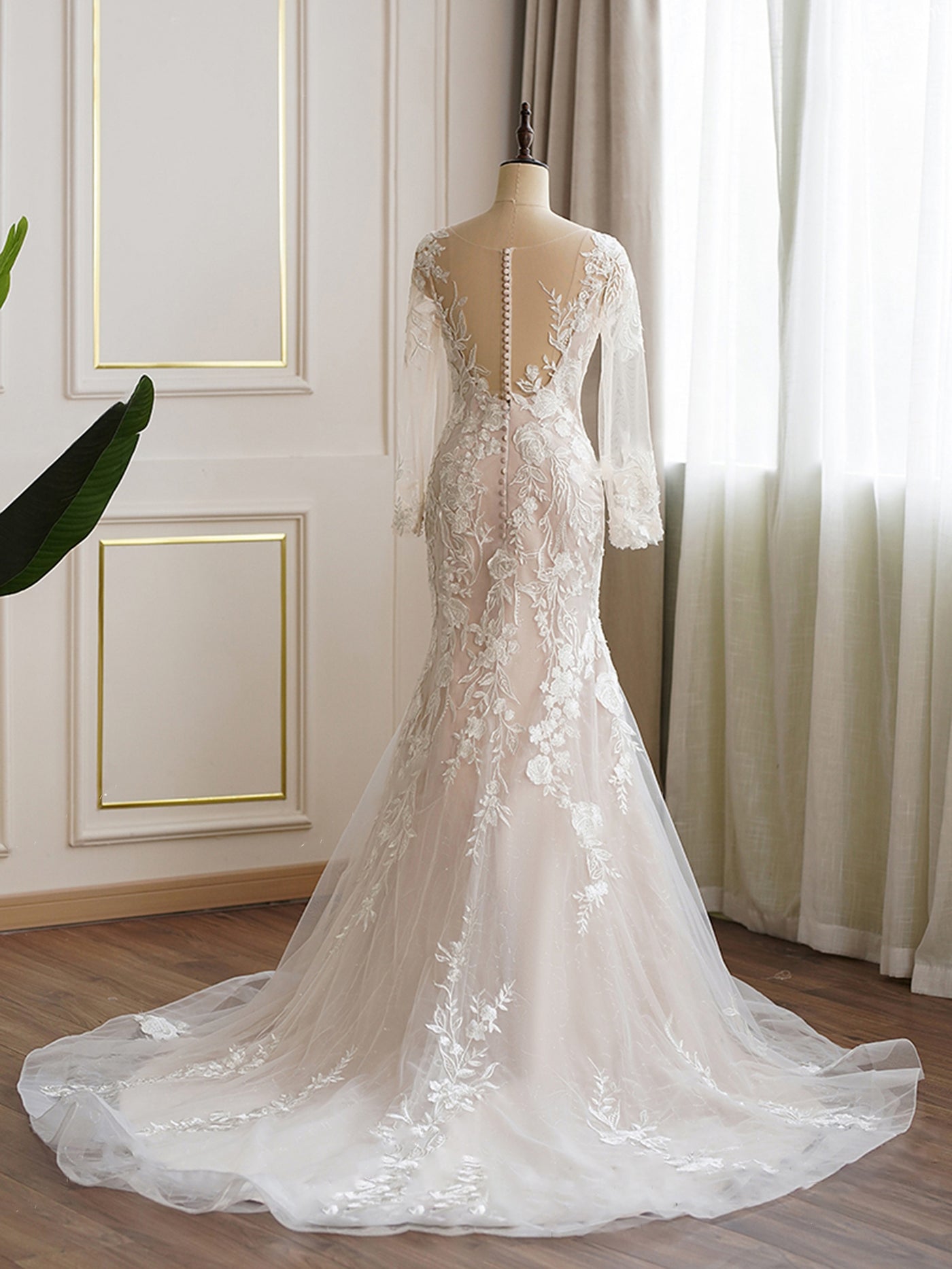 An elegant bridal gown with lace appliqué and illusion sleeves displayed on a mannequin. Ultimate Floral Fit and Flare Long Sleeve Wedding Dress - Off The Rack by Bergamot Bridal.