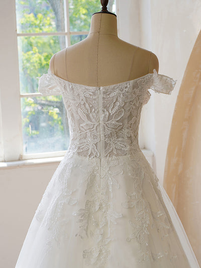 An Off the Shoulder Lace With Floral Wedding Dress from Bergamot Bridal in front of a window at a bridal shop in London.