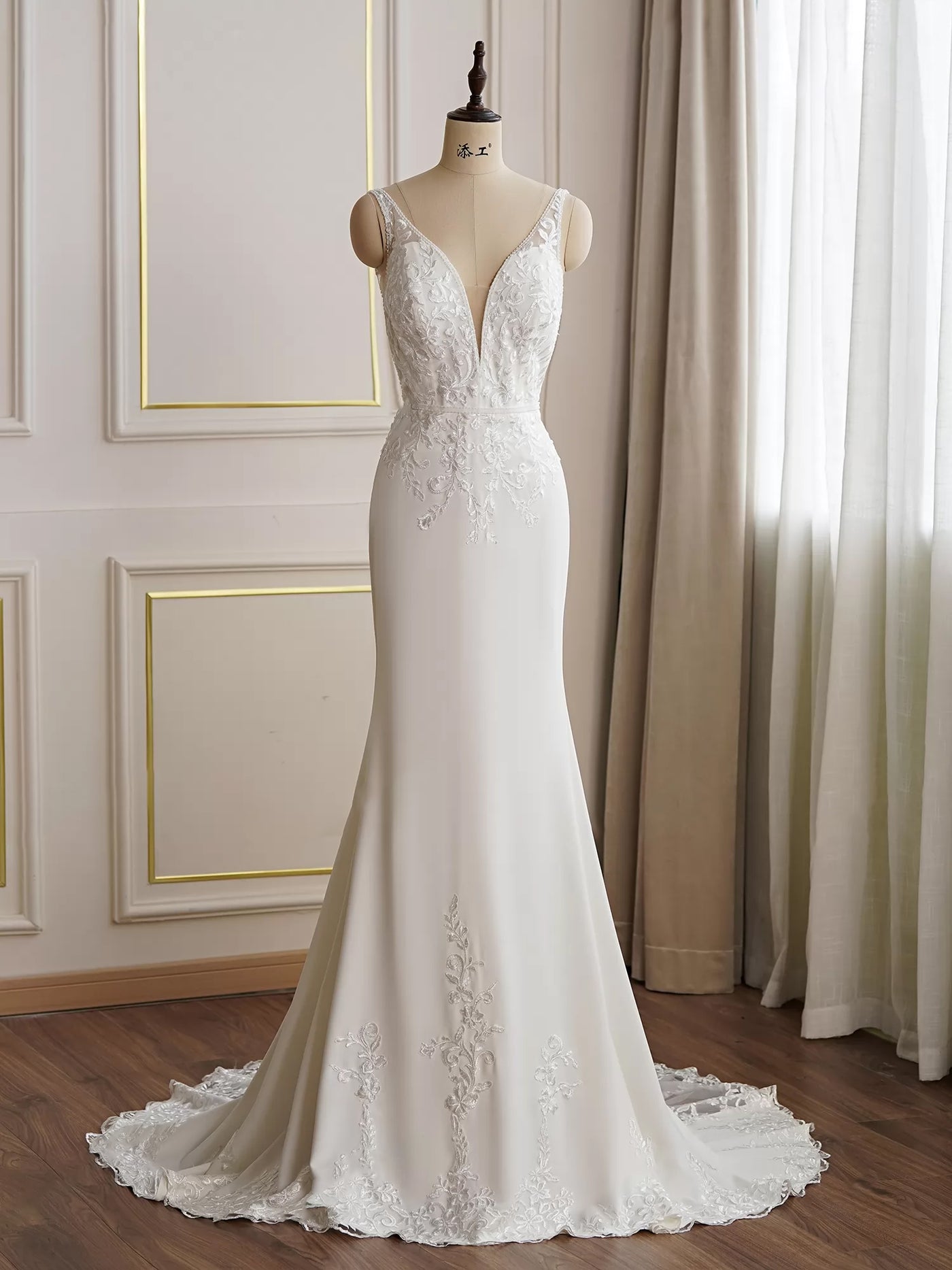 An elegant white wedding dress with lace detailing and a long train, displayed on a mannequin in a sophisticated Bergamot Bridal shop setting.