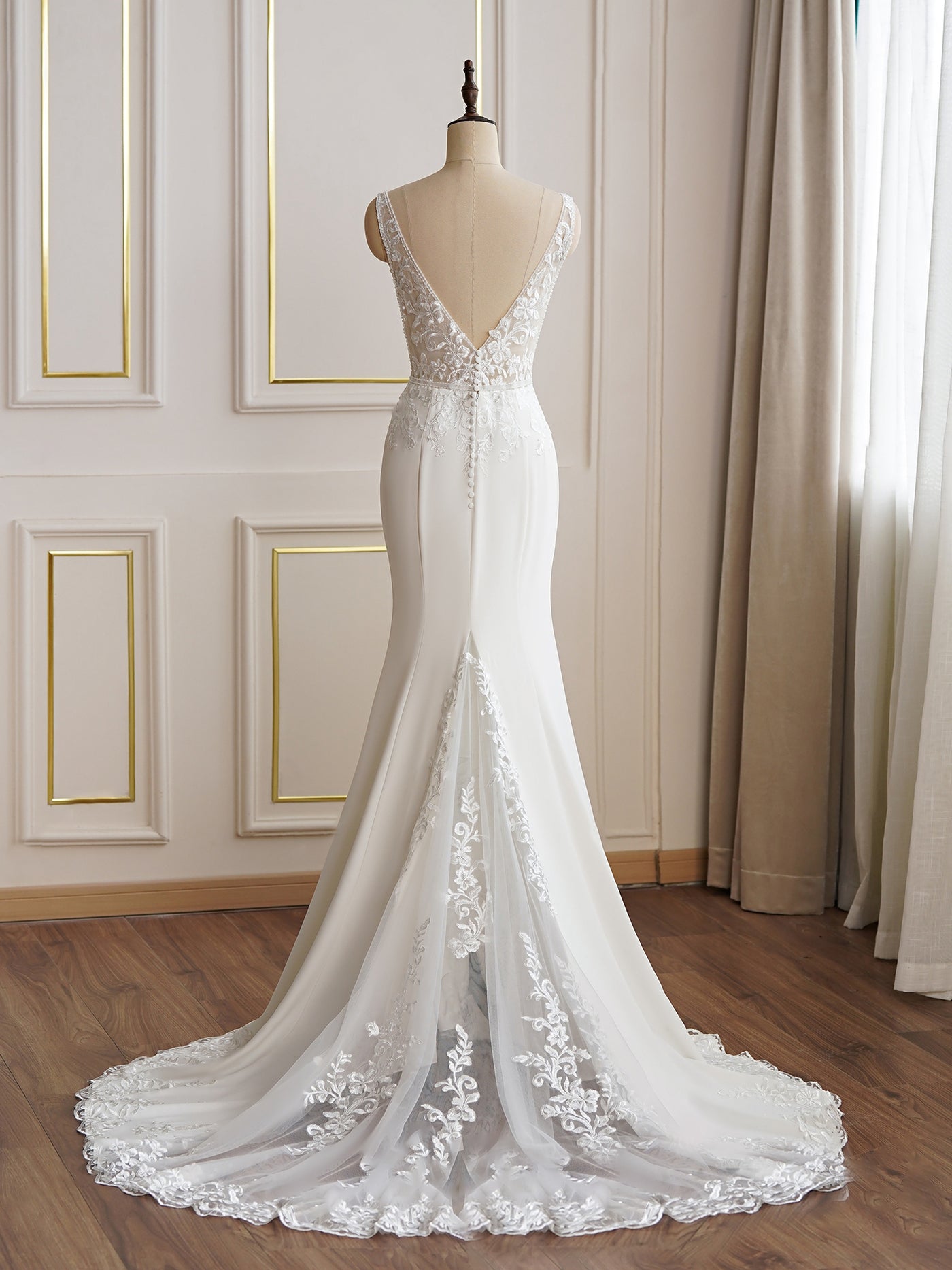 A white Beaded Lace Fit and Flare Bridal Gown with lace detailing and a long train, displayed on a mannequin in a Bergamot Bridal shop with elegant white paneling.