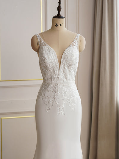 A mannequin in a bridal shop displays a Bergamot Bridal beaded lace fit and flare bridal gown with lace train, set against a soft curtain backdrop.