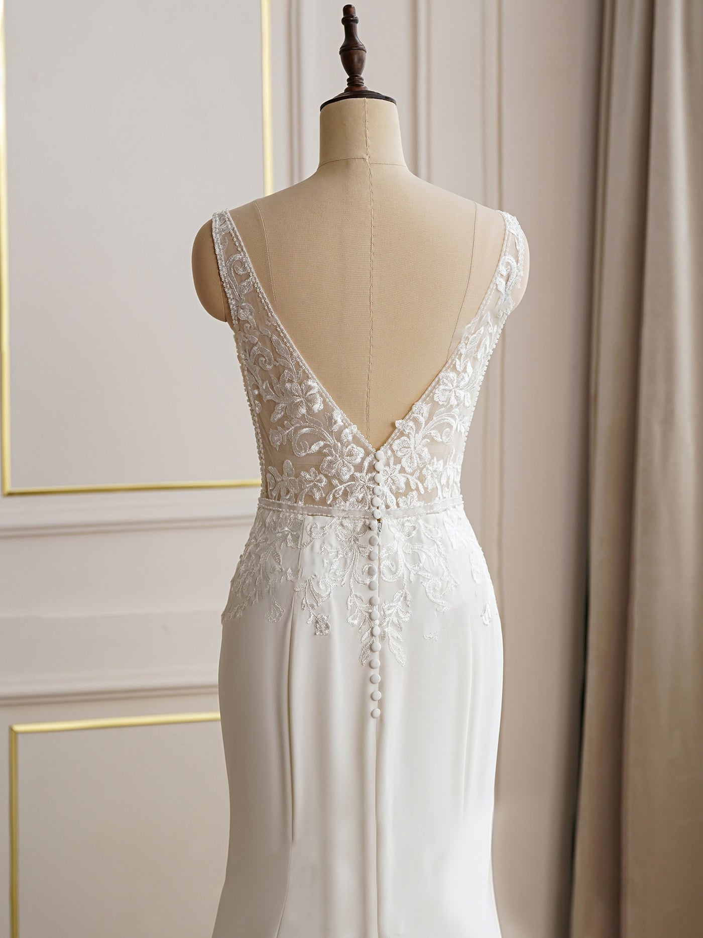 An elegant white wedding dress with lace detailing on a mannequin, featuring a deep v-back and intricate floral embroidery, available at Bergamot Bridal shops in London.