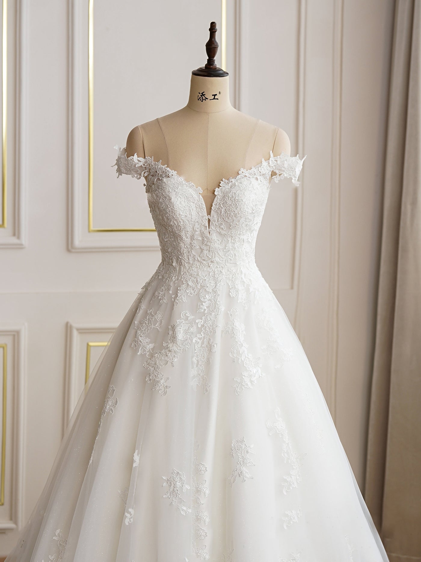 An Elegant Lace A-line Wedding Dress With Off the Shoulder Sleeves by Bergamot Bridal in a bridal shop.