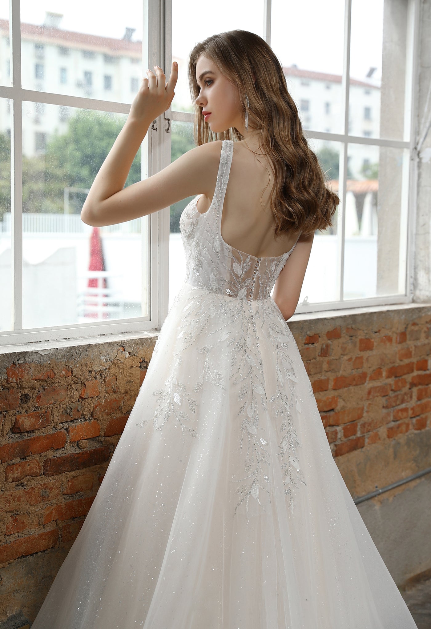 A woman in a Bergamot Bridal Square Neckline Wedding Dress with Delicate Leafy Lace looking out of a window in London.