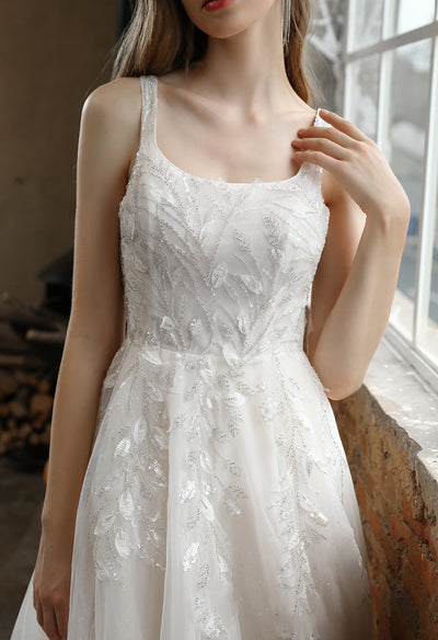 A woman in a white Bergamot Bridal wedding dress posing by a window at a bridal shop in London, wearing the Square Neckline Wedding Dress with Delicate Leafy Lace dress.