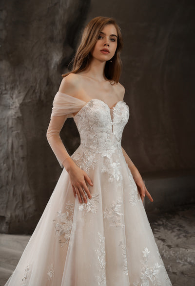 The bride is wearing a white Off-the-Shoulder Romantic Wedding Ball Gown with Glamorous Floral Motifs from Bergamot Bridal with long sleeves.