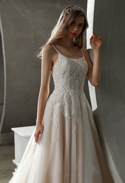 A bride in a Beaded Lace A-line Wedding Gown with Scoop Neckline by Bergamot Bridal leaning against a wall.